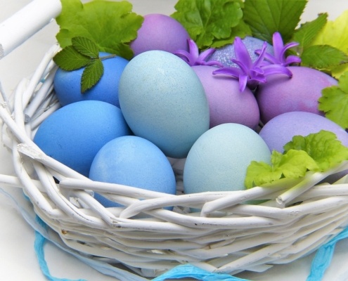 Ostermenü - Weißes Osterkörbchen mit lila, blauen, und hellblauen Eiern, dazu Blätter als Dekoration