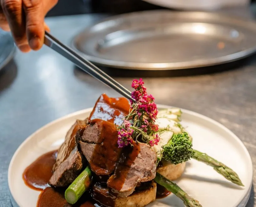 Koch gießt mit Soßenkelle Soße über den angerichteten Braten