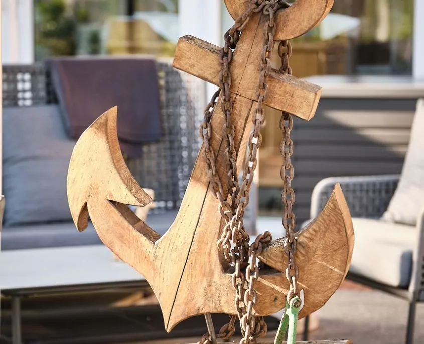 Brauner Anker aus Holz mit einer echten Kette, dahinter Stühle von Terrasse